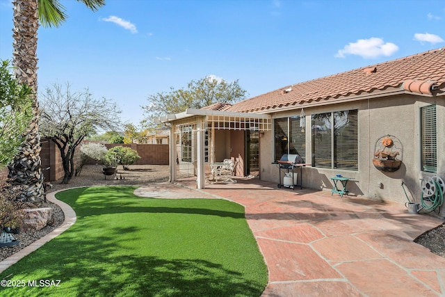 rear view of property featuring stucco siding, a lawn, a patio area, a fenced backyard, and a tiled roof