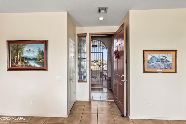 interior space with light tile patterned floors, a textured ceiling, visible vents, and baseboards