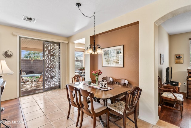 dining room featuring arched walkways, light wood-style flooring, visible vents, and an inviting chandelier