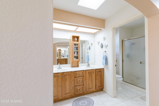 bathroom featuring double vanity, a sink, toilet, and a shower stall