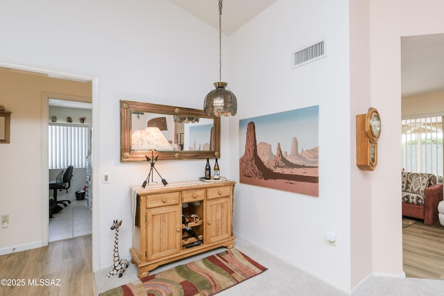 corridor featuring light wood-style floors, baseboards, visible vents, and high vaulted ceiling