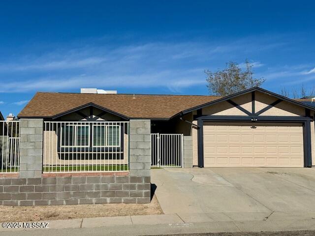 ranch-style home featuring a fenced front yard, driveway, a shingled roof, and an attached garage