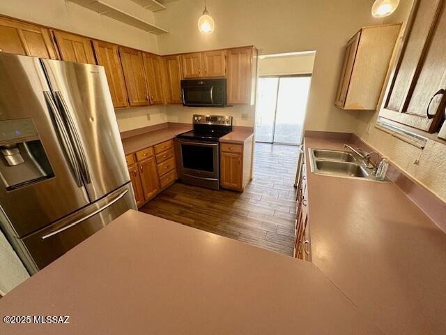 kitchen featuring dark wood-style floors, stainless steel appliances, light countertops, hanging light fixtures, and a sink