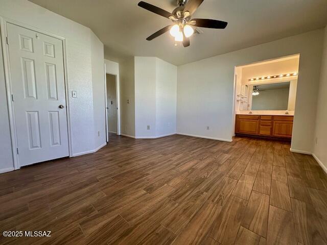 unfurnished bedroom featuring ceiling fan, baseboards, dark wood finished floors, and ensuite bathroom