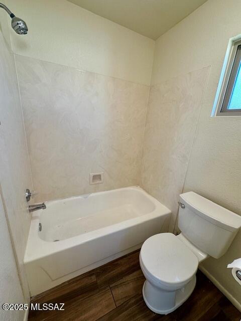 bathroom with bathtub / shower combination, toilet, and wood finished floors