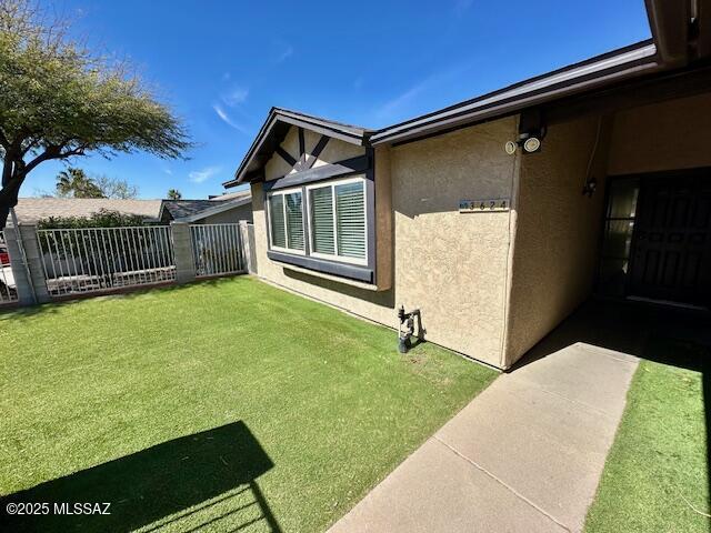 view of side of property featuring a lawn, fence, and stucco siding