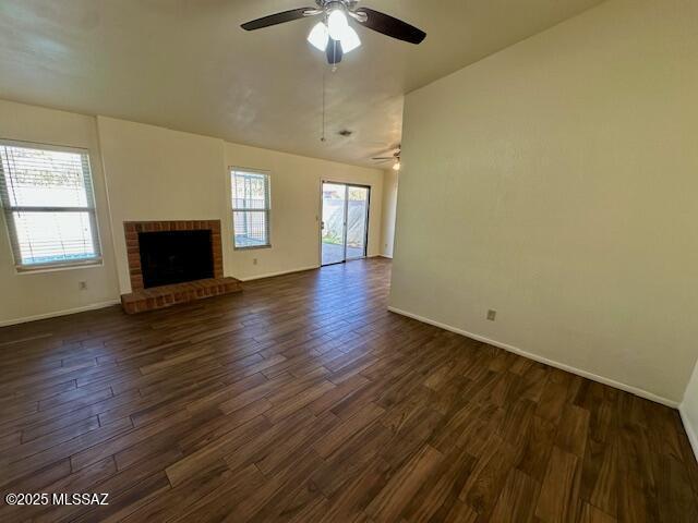 unfurnished living room featuring a fireplace, dark wood-type flooring, a ceiling fan, vaulted ceiling, and baseboards