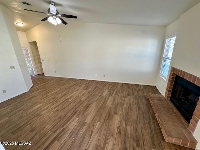 unfurnished living room featuring visible vents, a ceiling fan, dark wood-type flooring, vaulted ceiling, and a brick fireplace