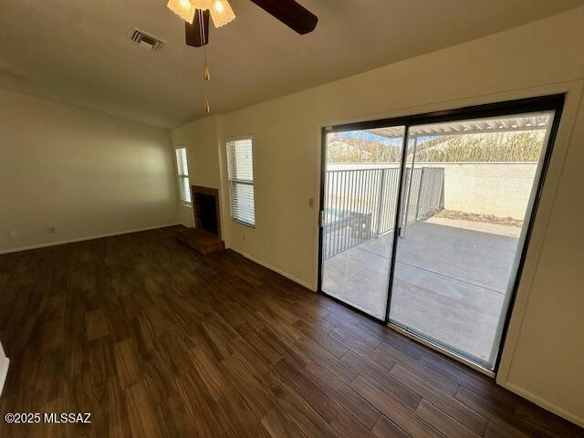 spare room featuring dark wood-type flooring, visible vents, a fireplace with raised hearth, and a ceiling fan