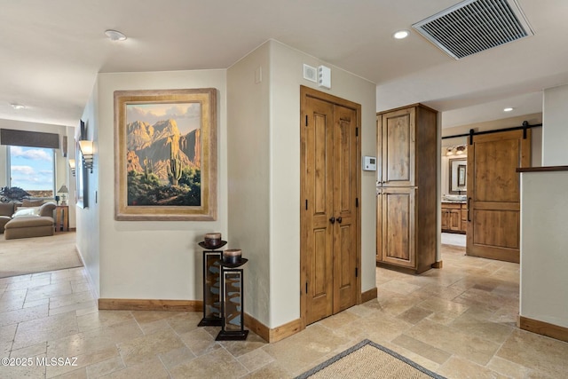 corridor with recessed lighting, stone tile flooring, visible vents, a barn door, and baseboards