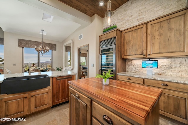 kitchen with wine cooler, a sink, a kitchen island, brown cabinets, and light stone countertops