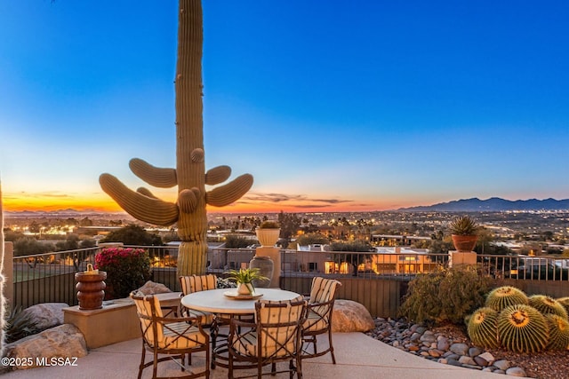 patio terrace at dusk with outdoor dining area, a mountain view, and fence