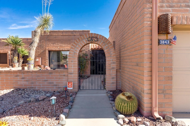 entrance to property with a garage, a gate, fence, and brick siding