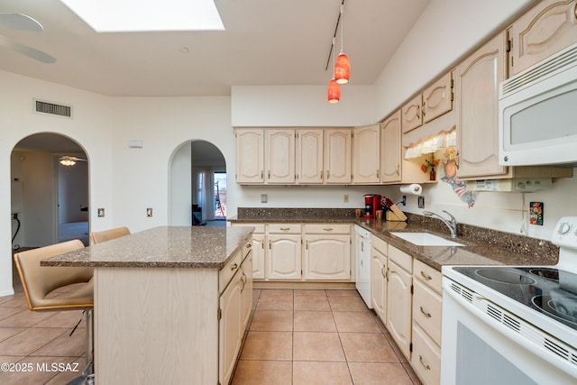 kitchen featuring arched walkways, a breakfast bar area, white appliances, a sink, and visible vents