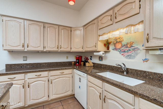 kitchen with dark stone countertops, light brown cabinetry, white dishwasher, and a sink