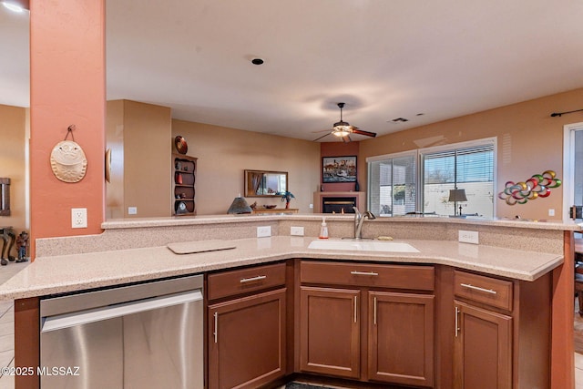 kitchen featuring a warm lit fireplace, brown cabinets, a peninsula, a sink, and stainless steel dishwasher