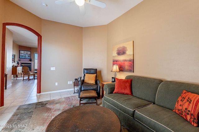 living room with light tile patterned floors, ceiling fan, arched walkways, a fireplace, and baseboards