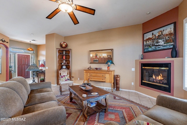 living area featuring light tile patterned floors, baseboards, a ceiling fan, and a glass covered fireplace