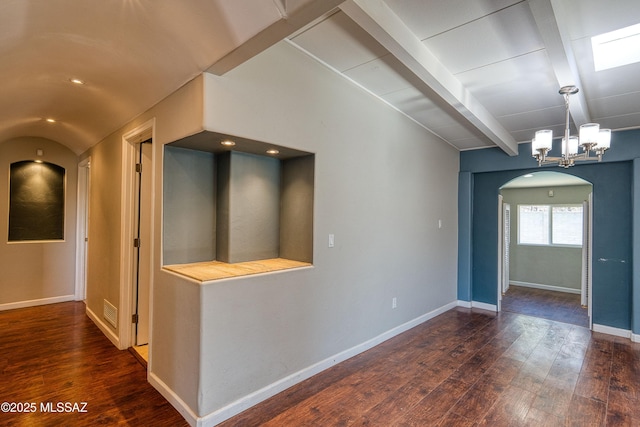 spare room with arched walkways, lofted ceiling with beams, hardwood / wood-style floors, an inviting chandelier, and baseboards