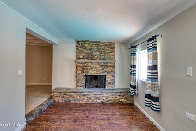 unfurnished living room featuring a stone fireplace, baseboards, and wood finished floors