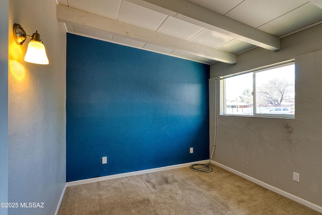 spare room featuring carpet, beam ceiling, and baseboards