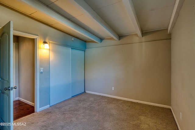 interior space featuring carpet floors, a closet, baseboards, and beamed ceiling