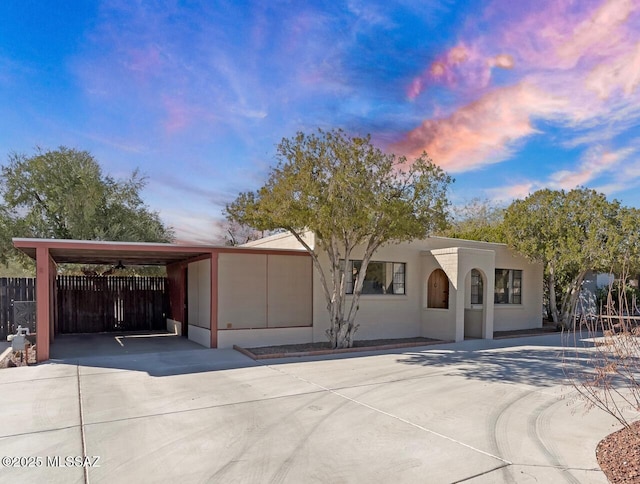 view of front of home with a carport, stucco siding, driveway, and fence