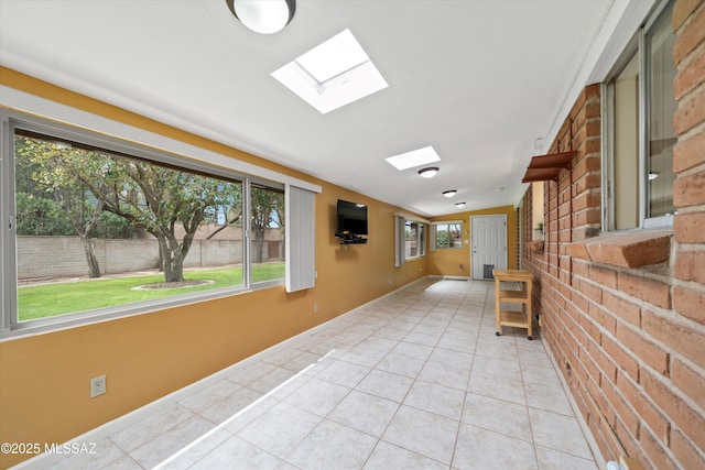 hallway featuring light tile patterned flooring, brick wall, a skylight, and baseboards