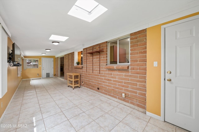 hall with light tile patterned floors, baseboards, a skylight, and brick wall