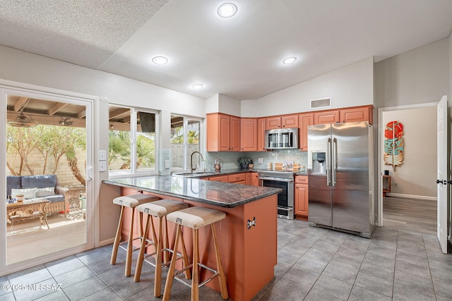 kitchen featuring stainless steel appliances, a peninsula, a sink, vaulted ceiling, and decorative backsplash