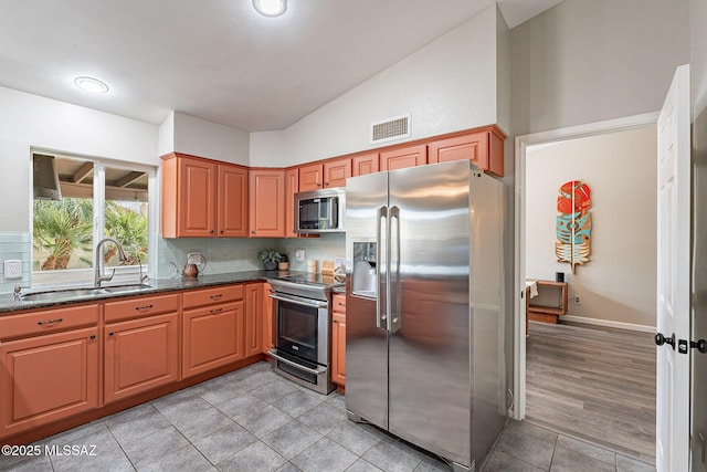 kitchen featuring stainless steel appliances, a sink, visible vents, backsplash, and dark stone counters