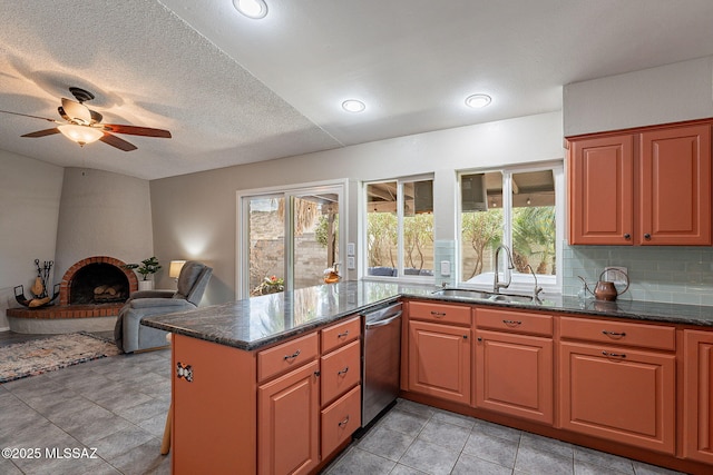 kitchen featuring decorative backsplash, dishwasher, a peninsula, a brick fireplace, and a sink