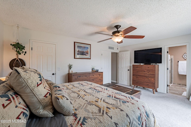 carpeted bedroom with a textured ceiling, ceiling fan, visible vents, and ensuite bathroom