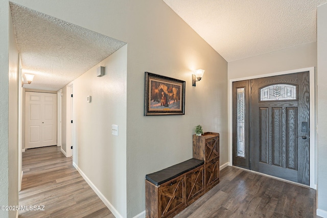 entrance foyer with vaulted ceiling, a textured ceiling, baseboards, and wood finished floors