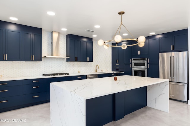 kitchen with light stone counters, a kitchen island, blue cabinetry, appliances with stainless steel finishes, and wall chimney range hood