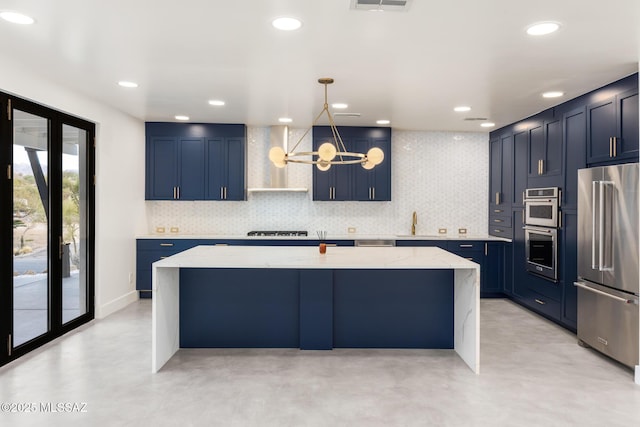 kitchen with blue cabinets, appliances with stainless steel finishes, wall chimney range hood, light stone countertops, and a chandelier