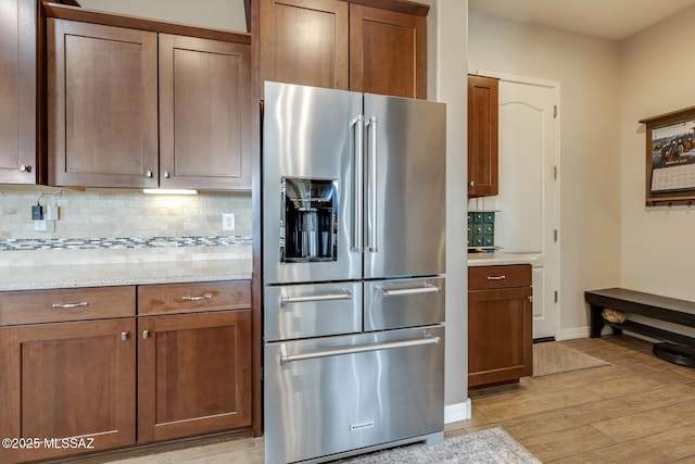 kitchen featuring baseboards, stainless steel fridge with ice dispenser, light stone counters, light wood-type flooring, and backsplash