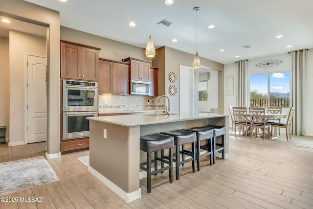 kitchen with a breakfast bar, stainless steel appliances, decorative backsplash, light wood-style floors, and a sink