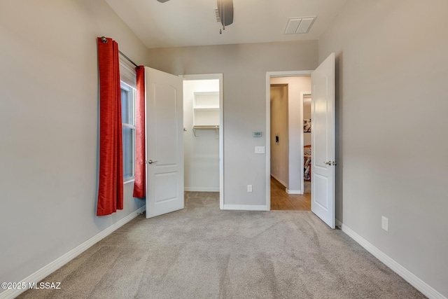 unfurnished bedroom featuring a ceiling fan, baseboards, visible vents, a walk in closet, and carpet flooring