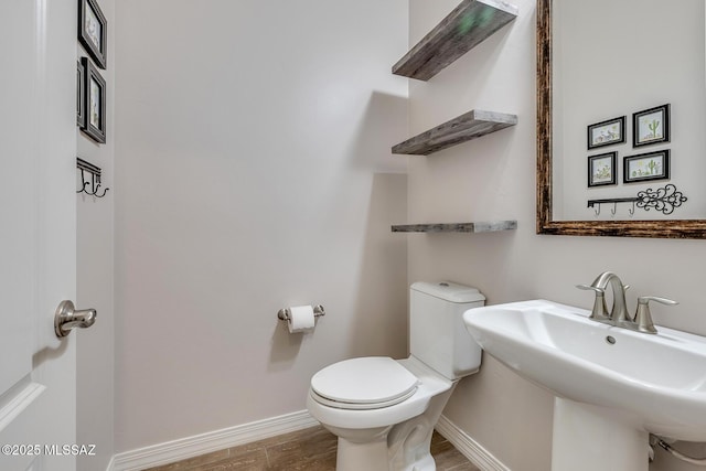 half bath featuring wood finished floors, a sink, toilet, and baseboards