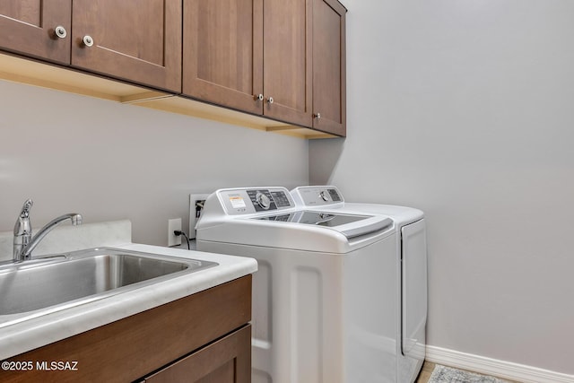 washroom with washer and dryer, cabinet space, a sink, and baseboards