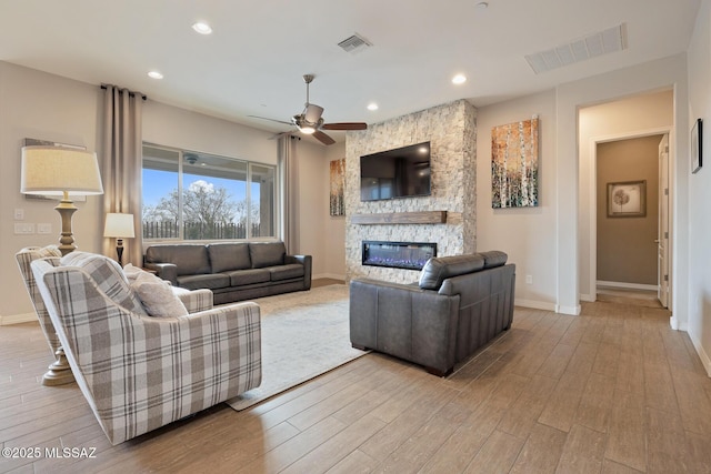 living area featuring visible vents, a stone fireplace, baseboards, and wood finished floors