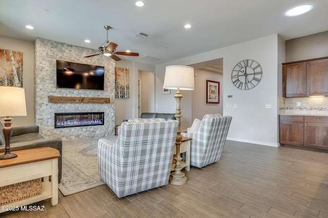 living room with a stone fireplace, visible vents, wood finished floors, and recessed lighting