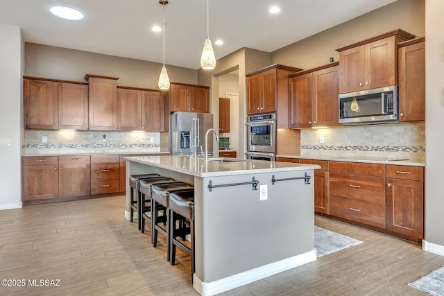 kitchen with a breakfast bar, stainless steel appliances, a sink, an island with sink, and light wood-type flooring