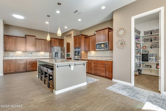 kitchen featuring light wood finished floors, visible vents, appliances with stainless steel finishes, brown cabinets, and a breakfast bar area