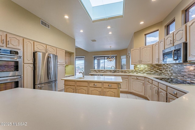 kitchen featuring stainless steel appliances, light countertops, decorative backsplash, a center island, and light brown cabinetry