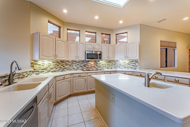 kitchen with appliances with stainless steel finishes, light countertops, a sink, and light brown cabinets