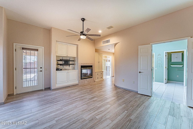 unfurnished living room with a fireplace, light wood finished floors, visible vents, ceiling fan, and baseboards