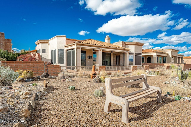 rear view of property with a tile roof, fence, a chimney, and stucco siding