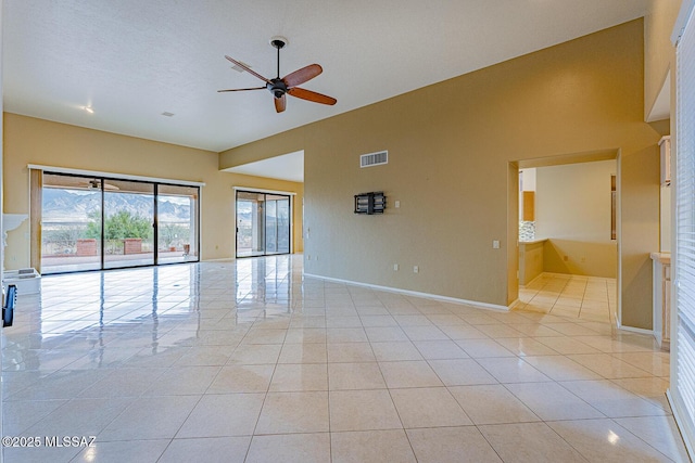 empty room featuring high vaulted ceiling, light tile patterned flooring, visible vents, and baseboards